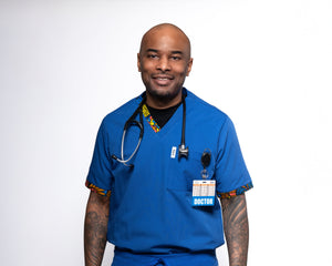 A man wearing a blue male scrub top with a V-neck and a single chest pocket, with a stethoscope around his neck.