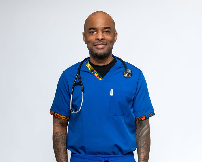 A man wearing a blue male scrub top with a V-neck and a single chest pocket, with a stethoscope around his neck.