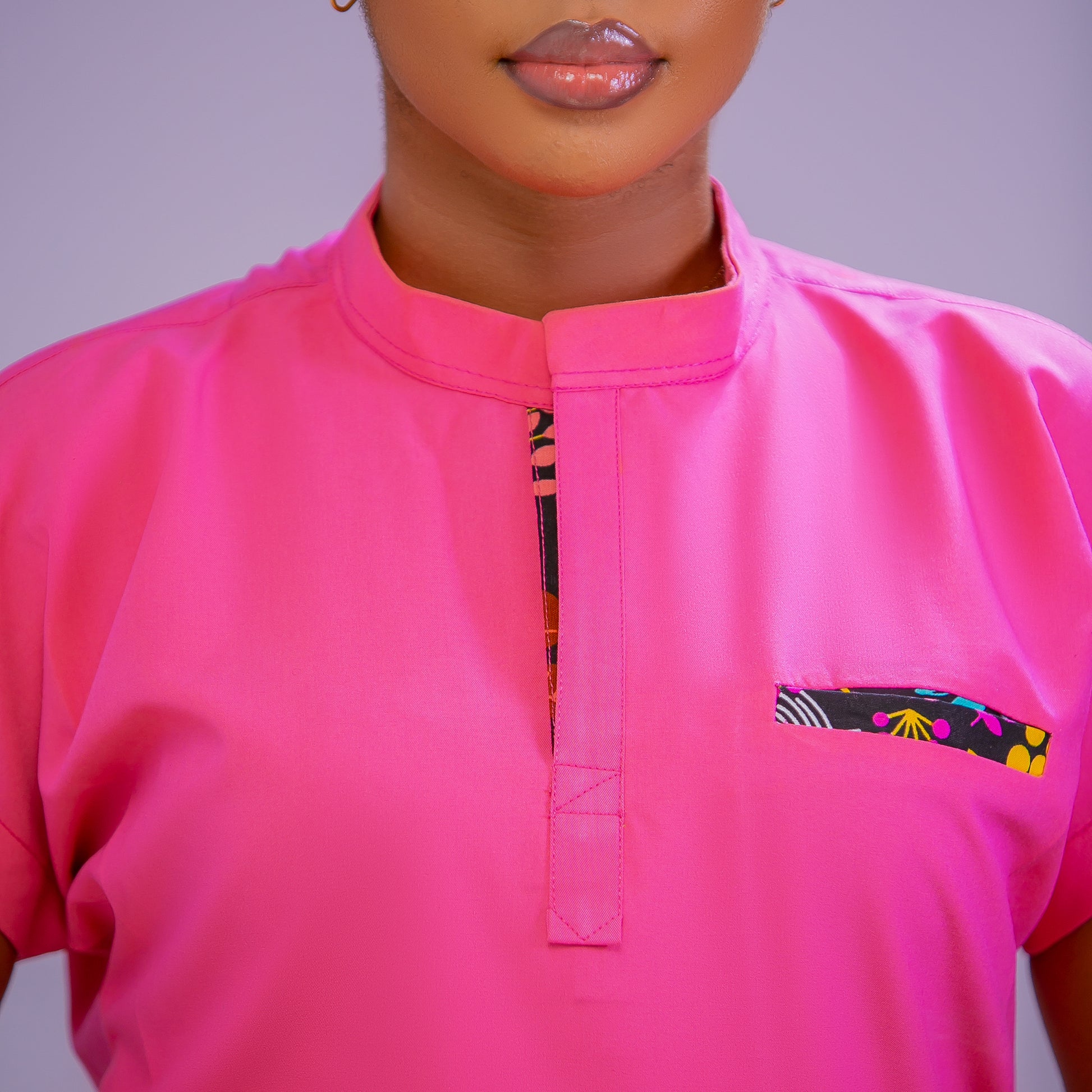 Person wearing a bright pink shirt with colorful pocket design on a plain background
