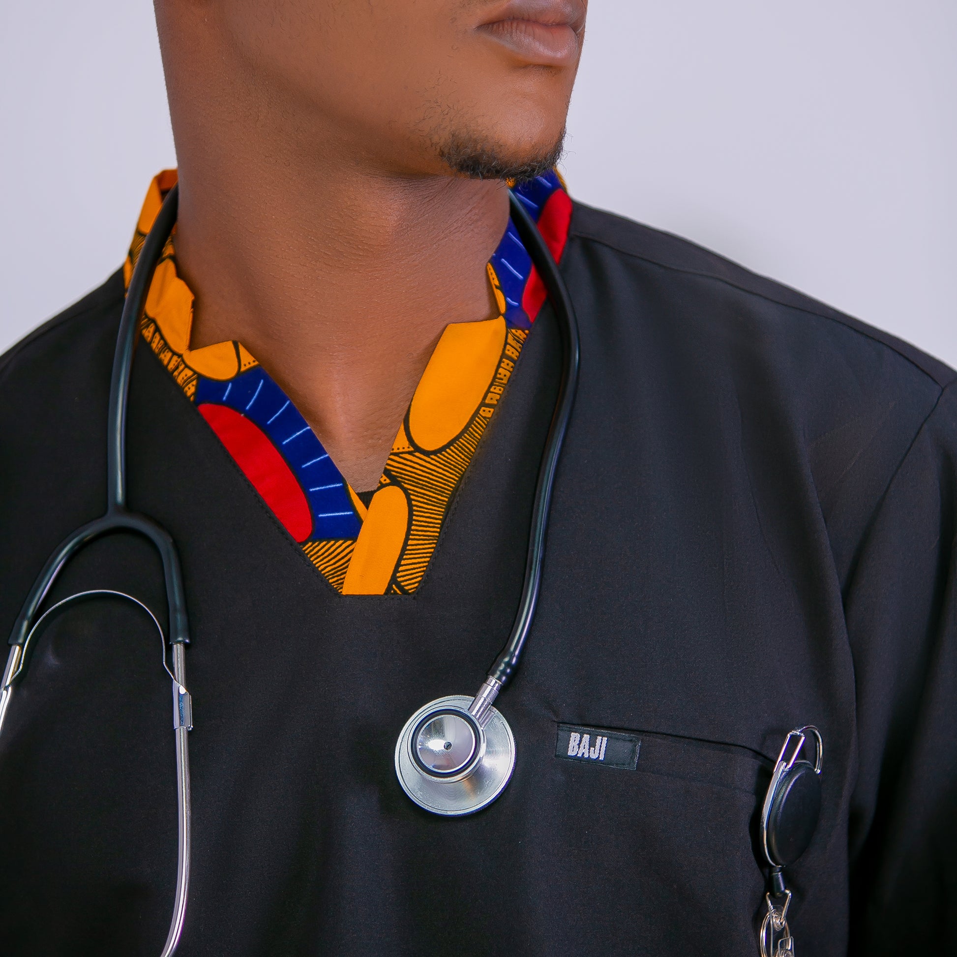 Person wearing a black scrub top with a colorful patterned stethoscope around their neck, on a plain background.