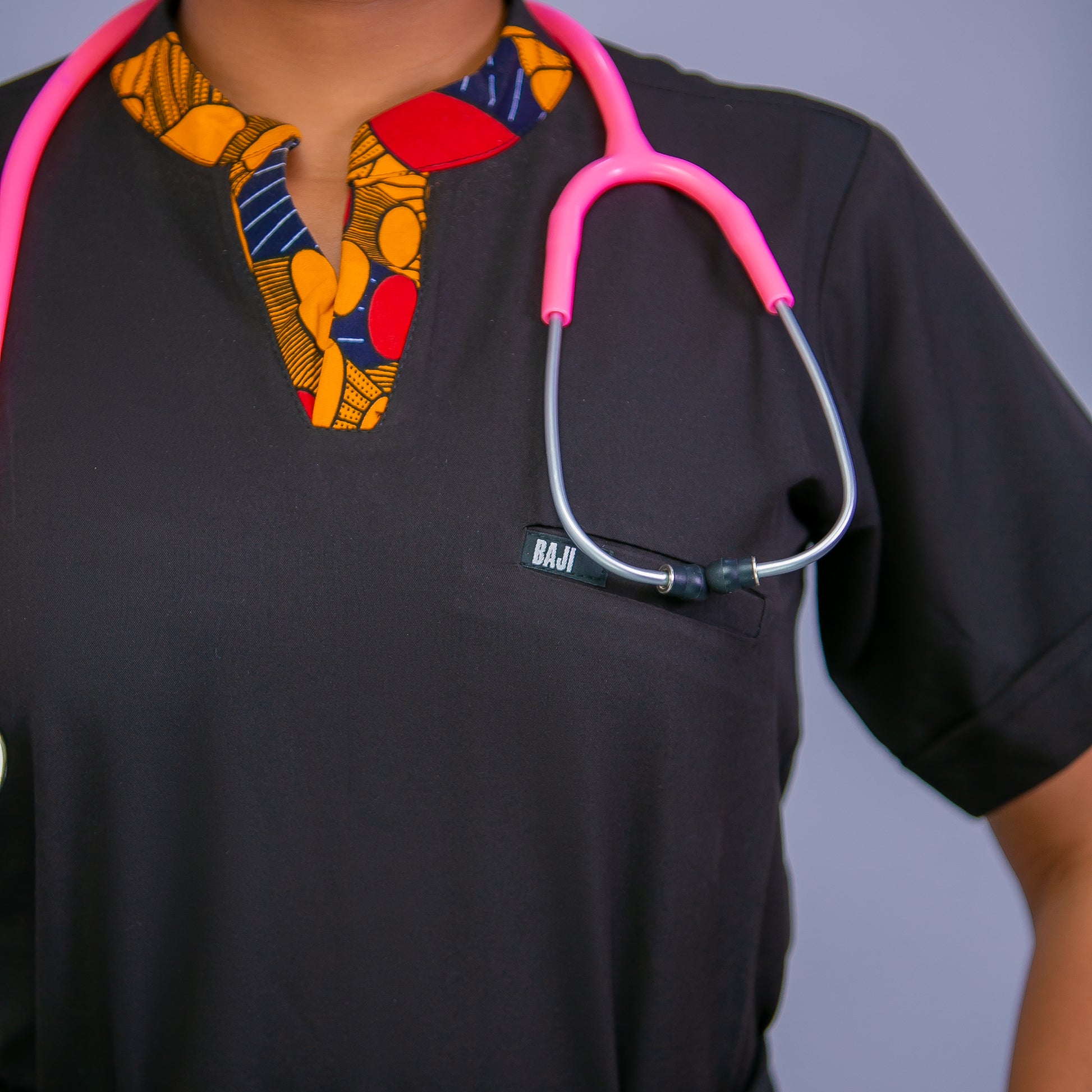 Person wearing a black scrub top with a colorful patterned collar and a pink stethoscope.
